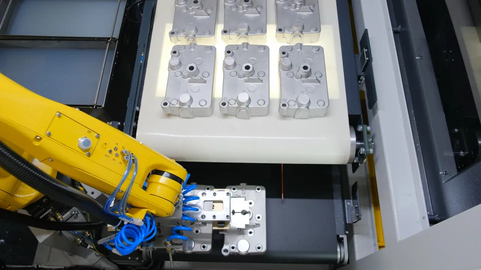 Machined housings lined up on the conveyor, the robot unloading the next one